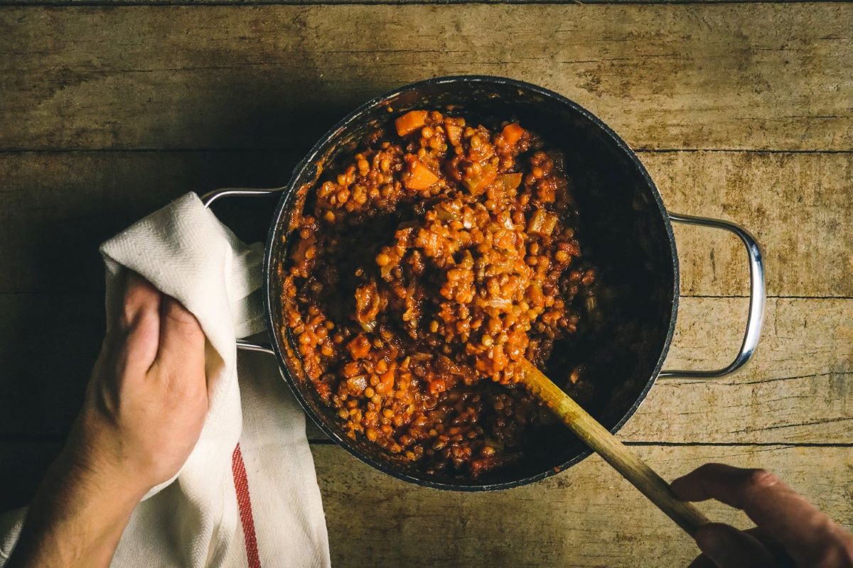 Photo of a man's hands stirring a pot of lentils and sweet potatoes
